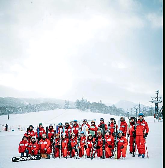 Instructors με κόκκινα jackets και κράνη σε πλατιά πλαγιά με lift στο βάθος