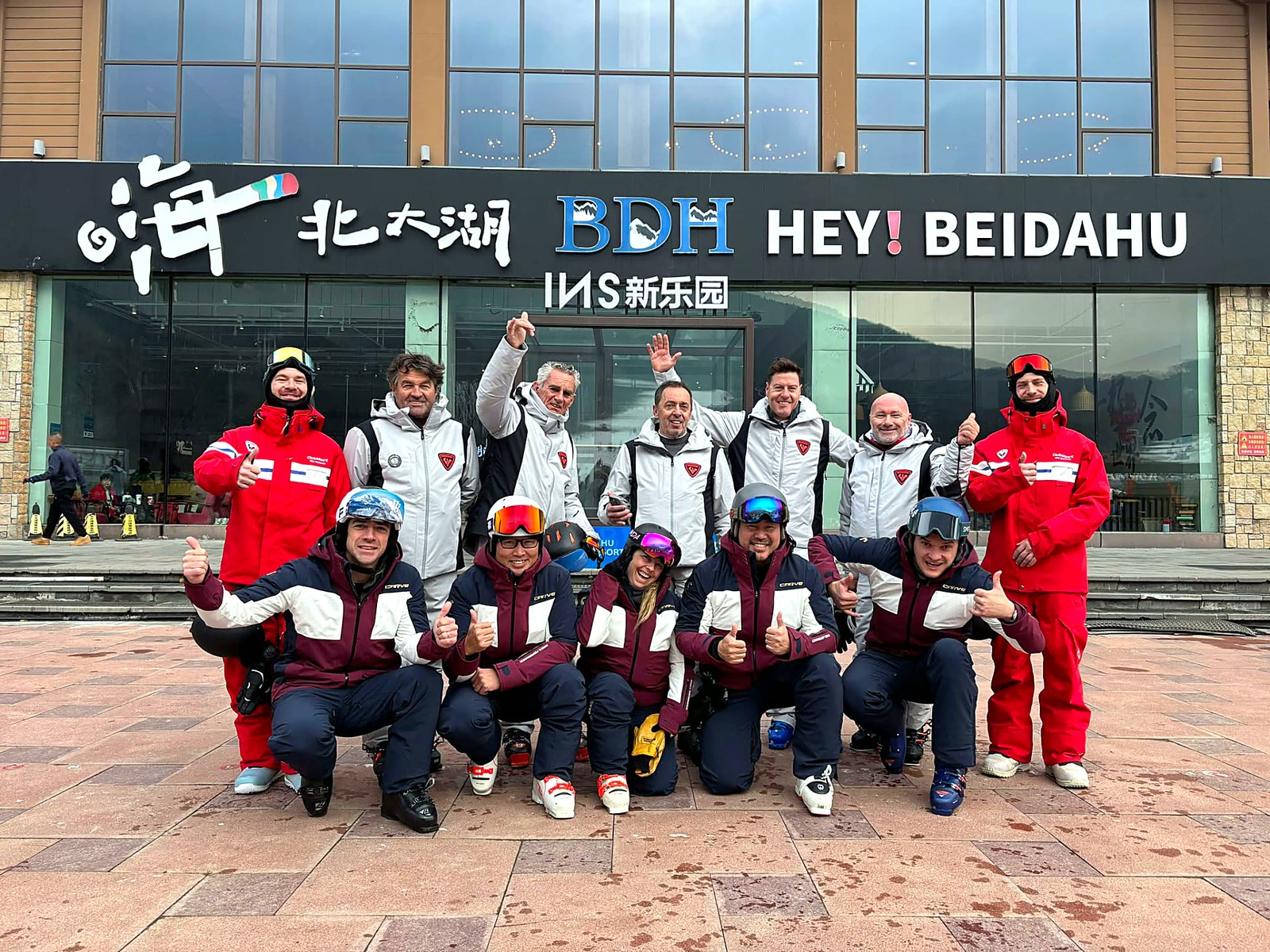 Ομάδα instructors με ομόμορφα jackets και κράνη φωτογραφημένη μπροστά στην είσοδο χιονοδρομικού κέντρου